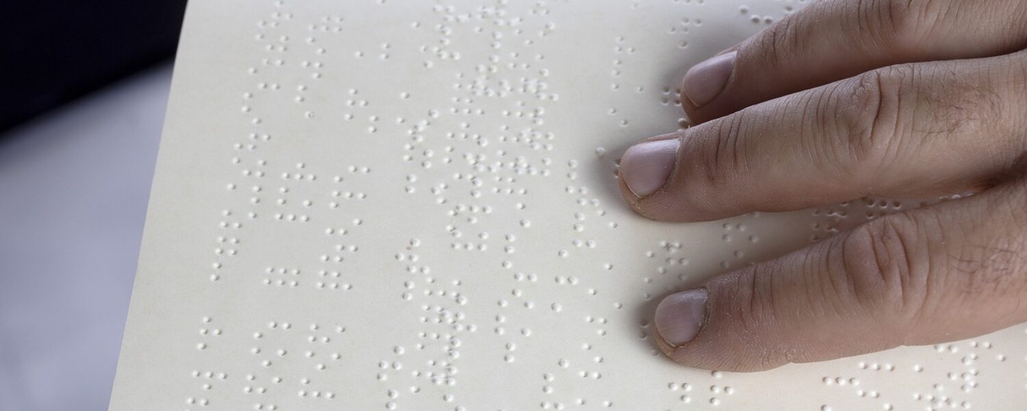 Person with fingers reading braille in book