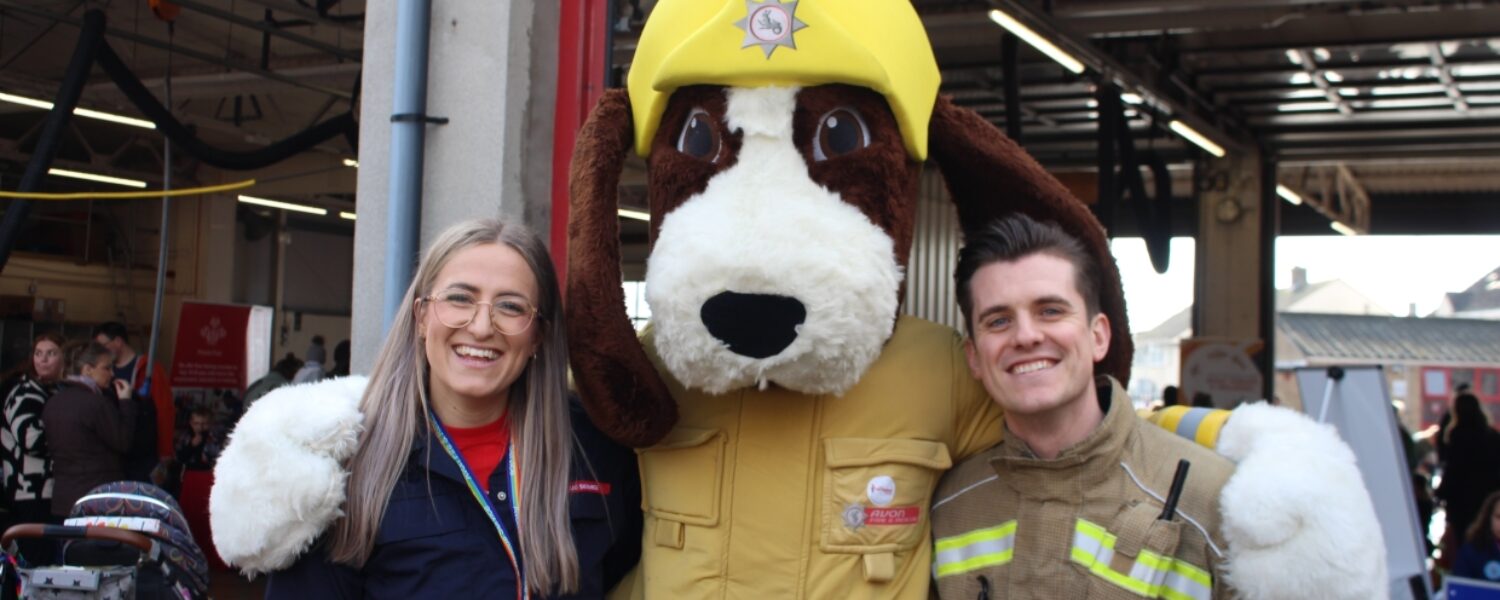 smiling blonde woman in glasses and red and blue uniform with Fido the fire dog mascot and male firefighter with brown hair
