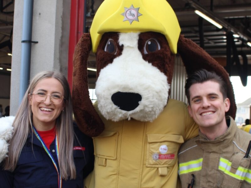 smiling blonde woman in glasses and red and blue uniform with Fido the fire dog mascot and male firefighter with brown hair