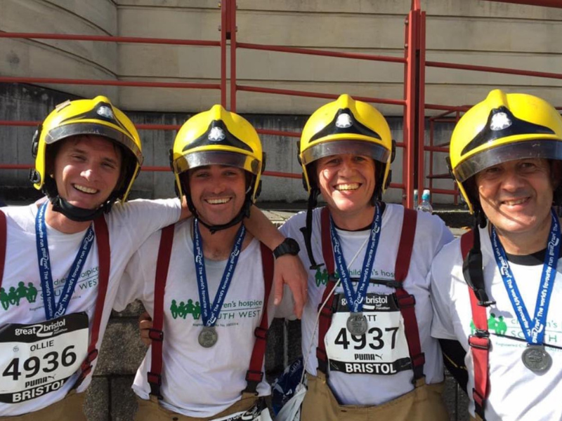group of firefighters wearing fire helmets and smiling with great bristol run t-shirts and medals on.
