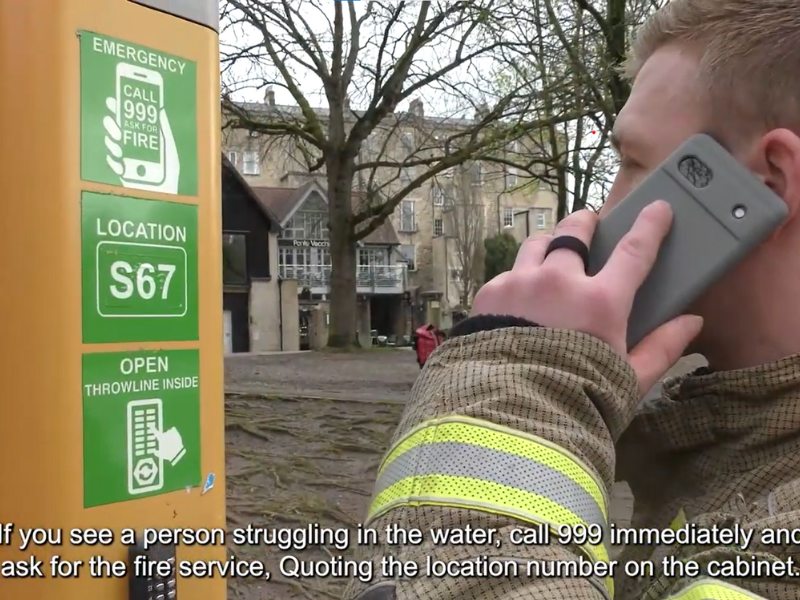 firefighter holding mobile phone calling 999 in front of river rescue cabinet box