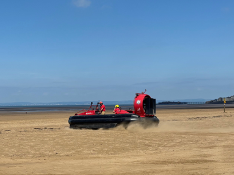 A fire service hovercraft is driving on the beach near the water