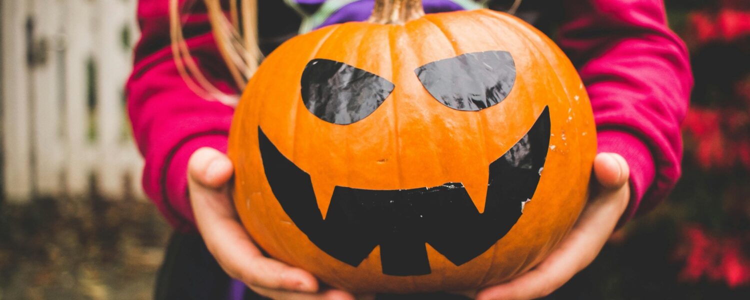 child wearing halloween witches costume while holding holiday pumpkin