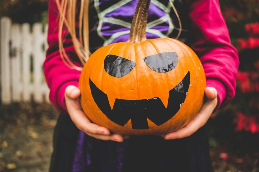 child wearing halloween witches costume while holding holiday pumpkin