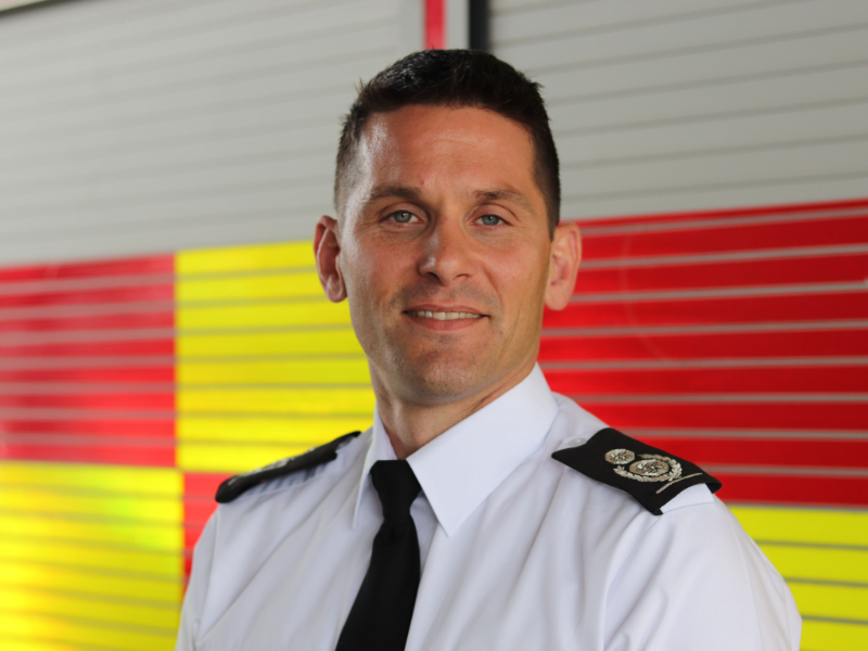 Chief Fire Officer Matt Cook stood in front of red and yellow fire engine.