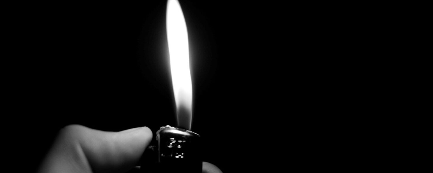 grayscale hand holding a gas lighter using the button to produce a flame