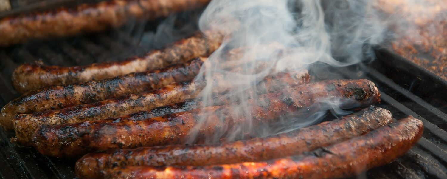 long chipolata sausages cooking on an outdoor grill